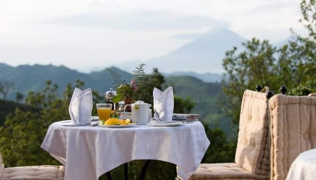 A luxury dining table set with white linens outdoors, featuring a backdrop of the majestic Virunga volcanoes