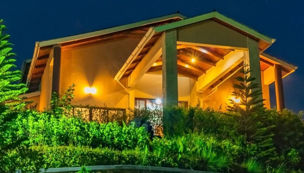 A large, modern stone lodge illuminated at night against the backdrop of the Bwindi hills.