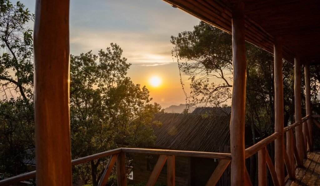 A sunset view from a wooden lodge porch looking out over the rolling ridges of the Bwindi forest.