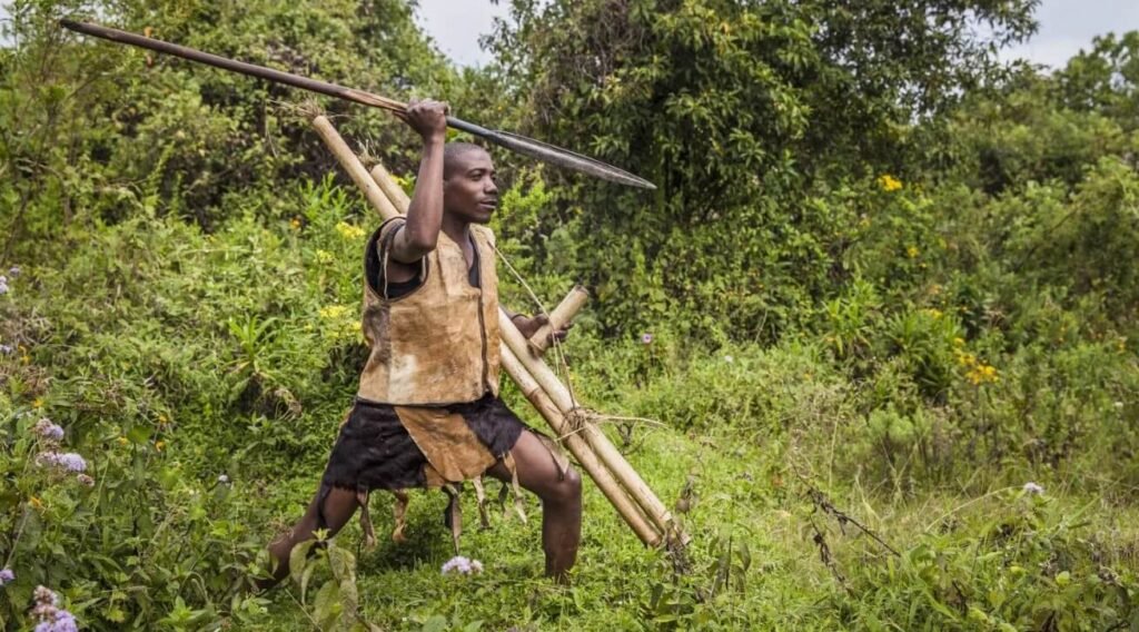 A Batwa man demonstrating traditional hunting techniques with a spear in the bush.