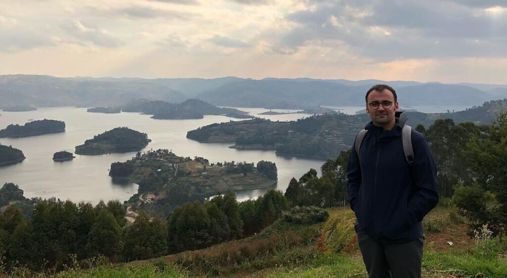 A silhouetted traveler watching the sunset over the scattered islands of Lake Bunyonyi from a high vantage point.
