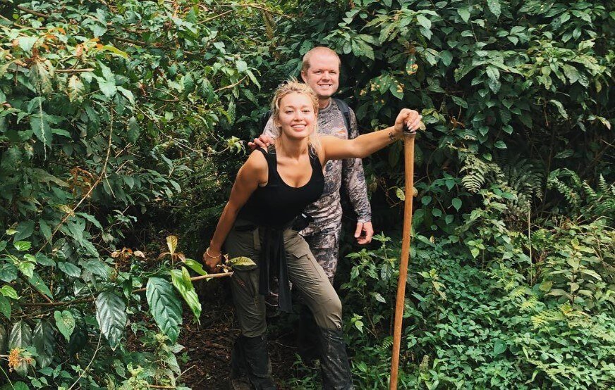 A man and woman using walking sticks to navigate a narrow, forested trail during a Bwindi gorilla trek