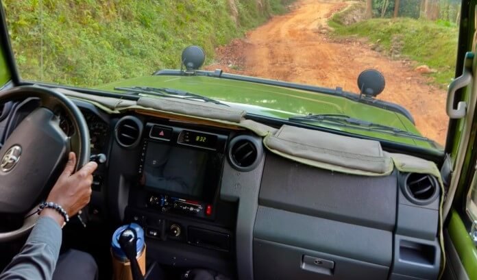 Perspective from the driver's seat of a safari vehicle on a winding dirt road through the Ugandan countryside.