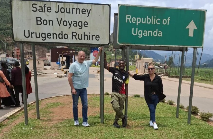 Tourists posing at the Katuna border post sign marked "Republic of Uganda," symbolizing the journey from Kigali.