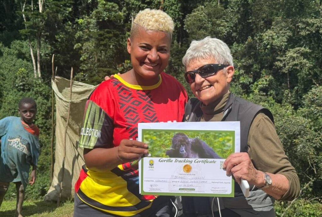 A traveler and a park official proudly holding up a signed "Gorilla Trekking Certificate" in front of a forest backdrop, marking the successful completion of the trek.
