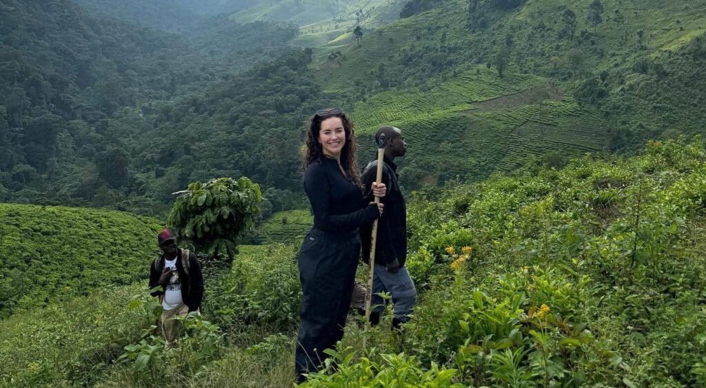 Hiker walking along a ridge with a stunning backdrop of the misty, terraced rolling hills characteristic of southwestern Uganda.