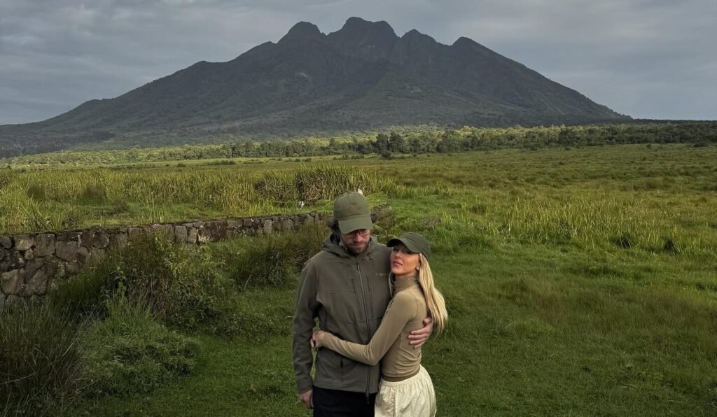 A couple embracing in a scenic valley with the towering Virunga Mountains in the background.