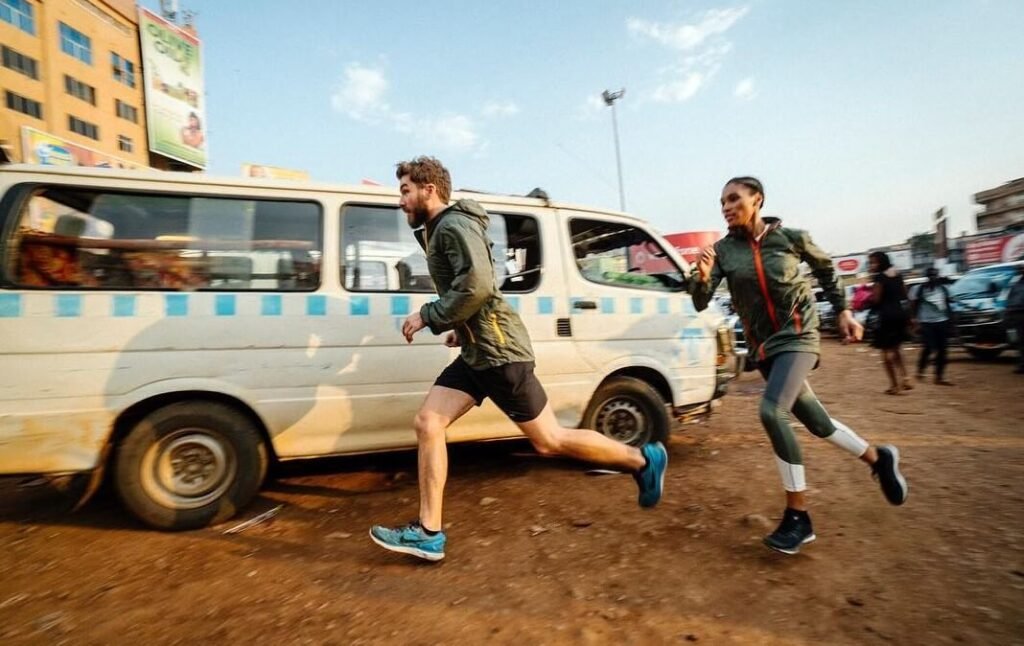 Two travelers running alongside a white commuter taxi in the dusty, sunlit Old Taxi Park in Kampala, capturing the fast-paced energy of Uganda’s primary transport hub.