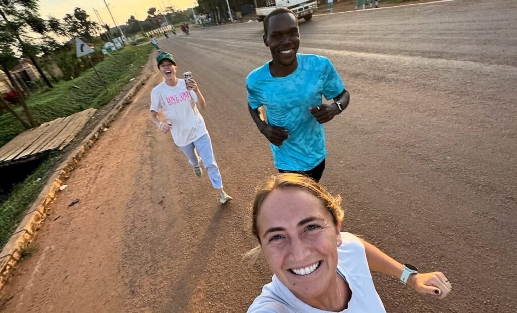 A wide-angle selfie of three people jogging along a red-dirt roadside in Gulu at sunrise, highlighting the safety and community feel of morning exercise in Northern Uganda.