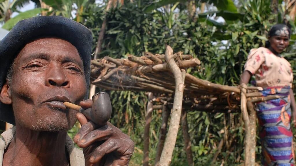 Close-up of a Batwa elder smoking a traditional wooden pipe during a cultural demonstration in Uganda.