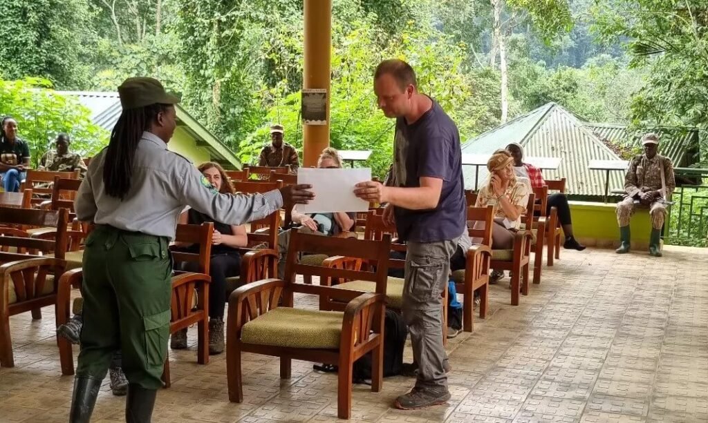 A proud traveler being handed an official gorilla trekking certificate by a park official at a safari lodge.