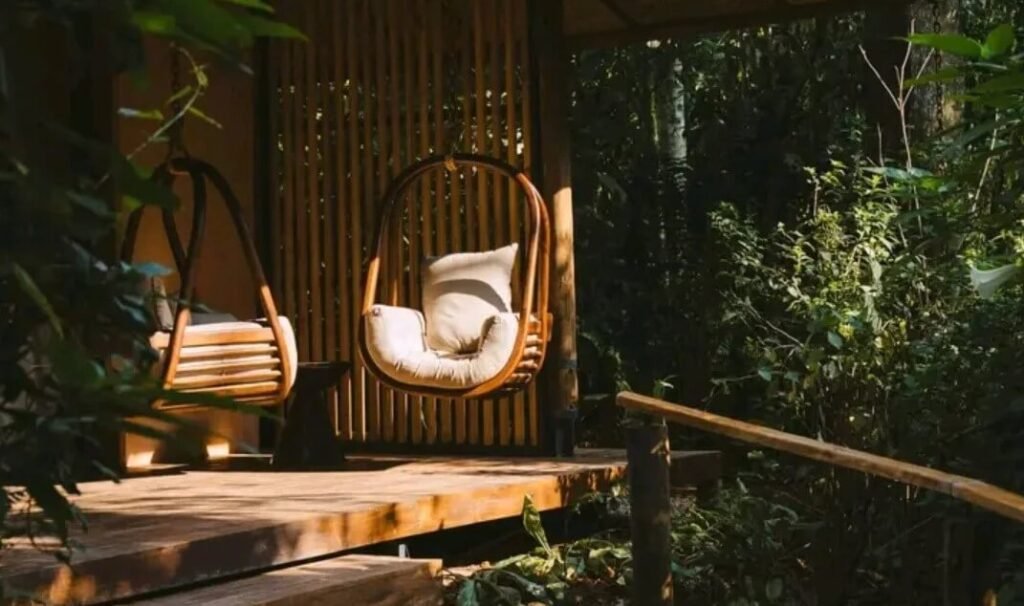 Cozy outdoor seating area with hanging basket chairs on a wooden deck surrounded by dense tropical greenery.