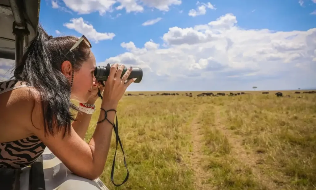 Teenage girl using binoculars to scan open savannah during a family safari in Uganda