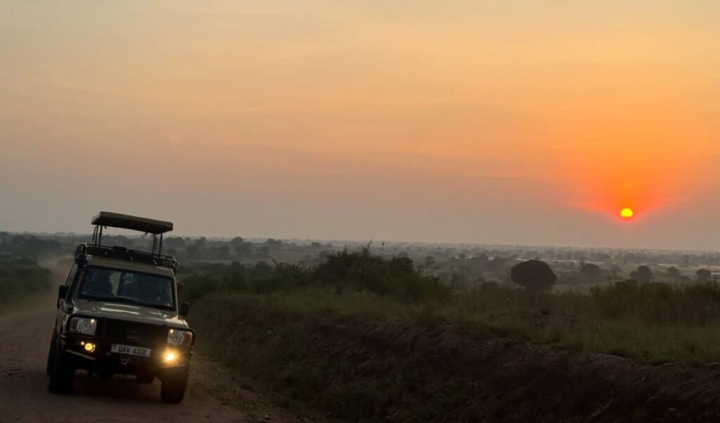 Silhouette of a safari vehicle on open savannah beneath a vivid orange and red Uganda sunset