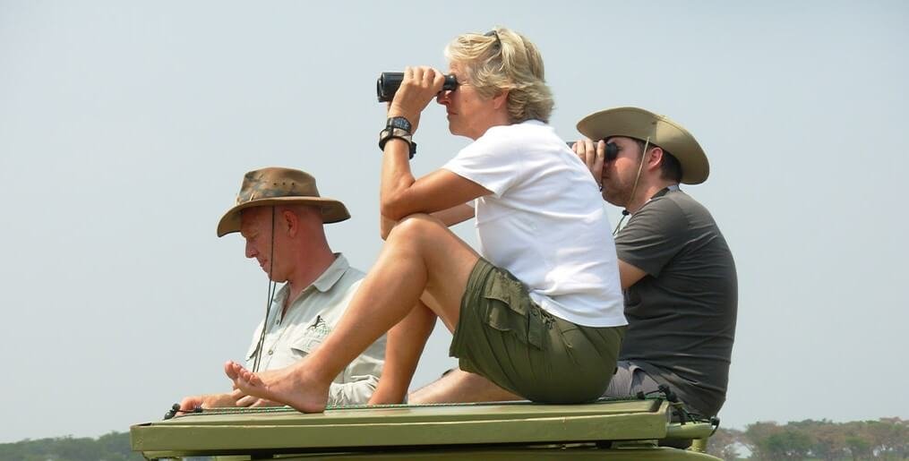 Two travelers using binoculars to spot birds from a safari vehicle during a birding trip in Uganda
