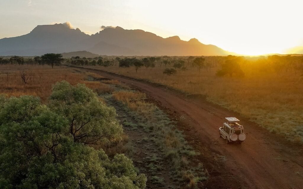 An aerial view of a safari vehicle driving along a dirt road through the misty hills of Bwindi at sunrise.