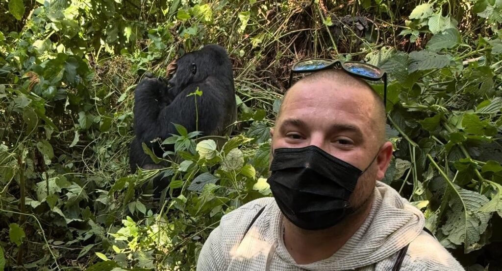 A man taking a selfie with a mountain gorilla just a few meters away in the forest.