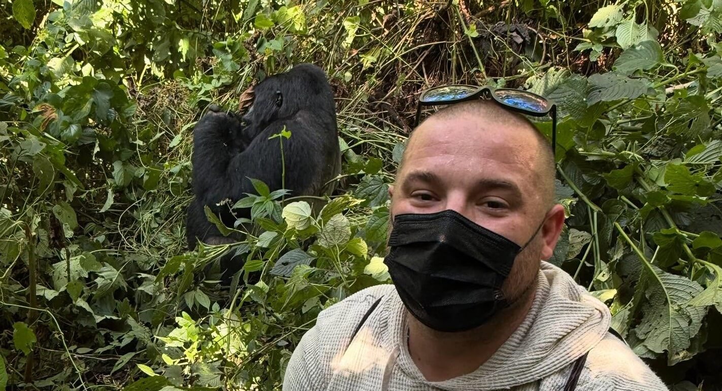 A man taking a selfie with a mountain gorilla just a few meters away in the forest.