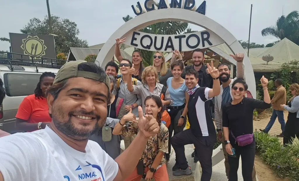 Group selfie of tourists celebrating together in front of the circular Uganda Equator sign at Kayabwe