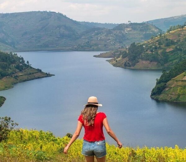 A traveler standing on a grassy hill overlooking the winding, deep blue waters and lush green islands of Lake Bunyonyi.