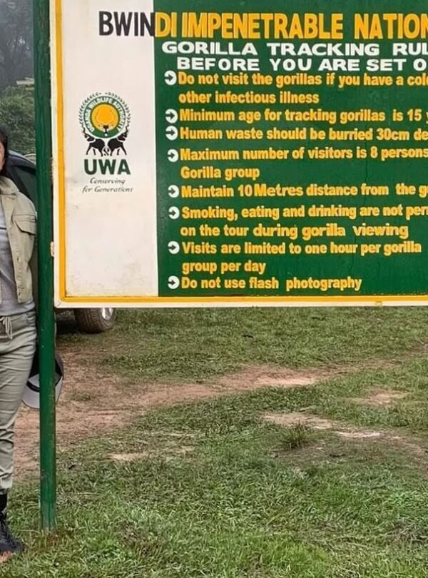 Two trekkers standing in front of the official wooden entrance sign for Bwindi Impenetrable National Park, marking the start of the trekking adventure.