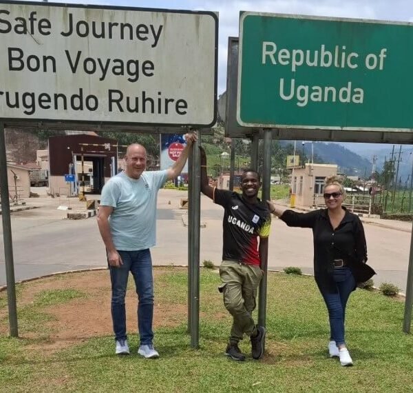 Tourists posing at the Katuna border post sign marked "Republic of Uganda," symbolizing the journey from Kigali.