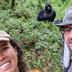 Close-up of happy trekkers with a mountain gorilla visible in the background forest.