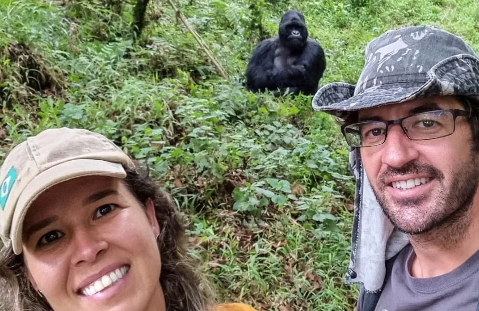 Close-up of happy trekkers with a mountain gorilla visible in the background forest.