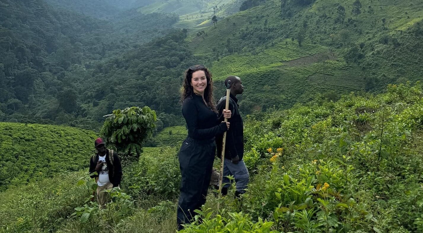 Hiker walking along a ridge with a stunning backdrop of the misty, terraced rolling hills characteristic of southwestern Uganda.