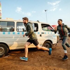 Two travelers running alongside a white commuter taxi in the dusty, sunlit Old Taxi Park in Kampala, capturing the fast-paced energy of Uganda’s primary transport hub.