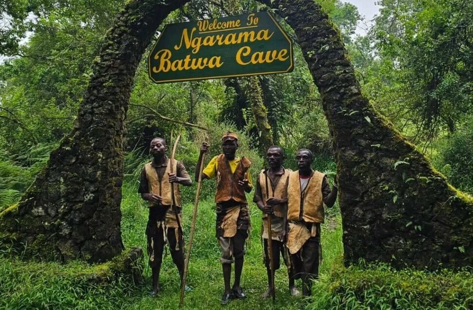 Stone archway entrance to the historic Garama Cave in Uganda with Batwa guides standing at the entrance.