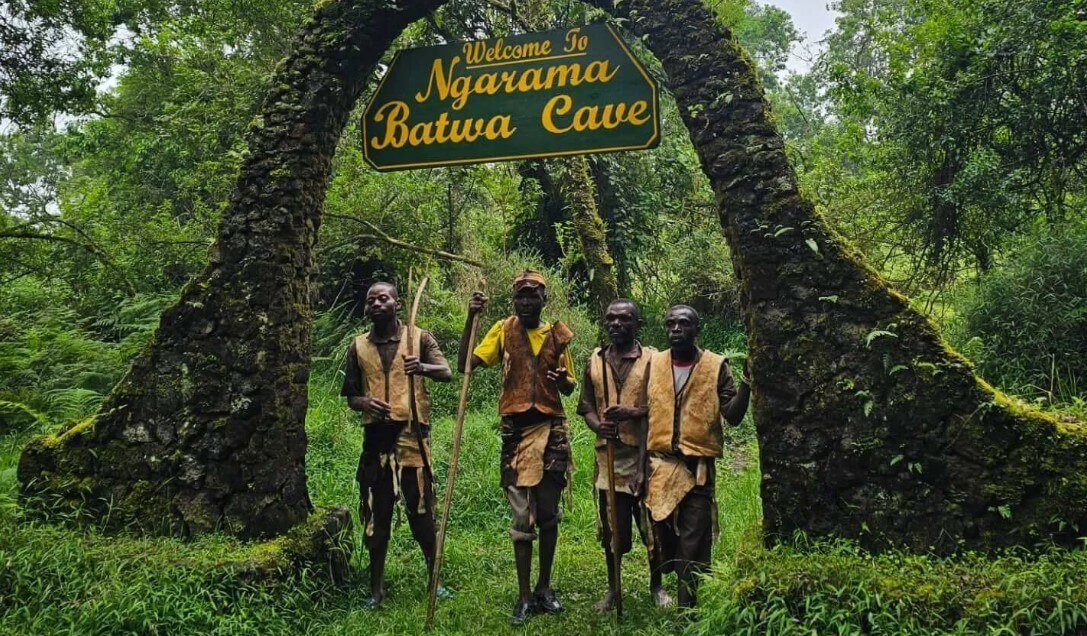 Stone archway entrance to the historic Garama Cave in Uganda with Batwa guides standing at the entrance.