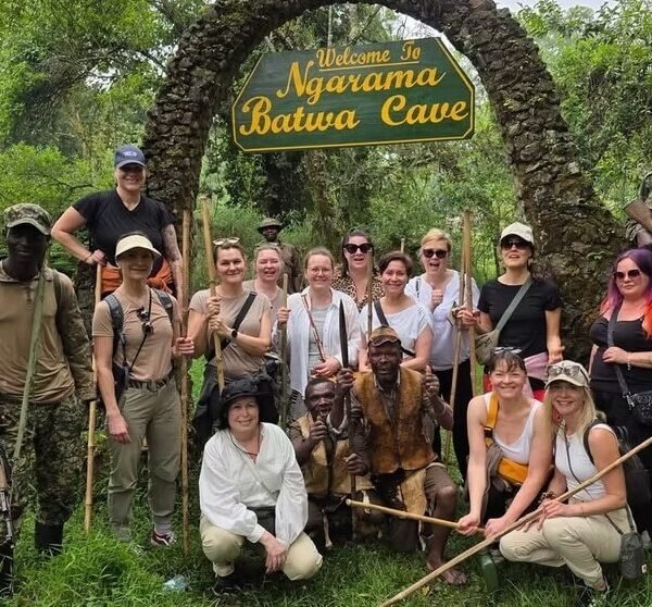A group of hikers and guides crossing a wooden footbridge over a stream during a trek in Bwindi Impenetrable Forest.