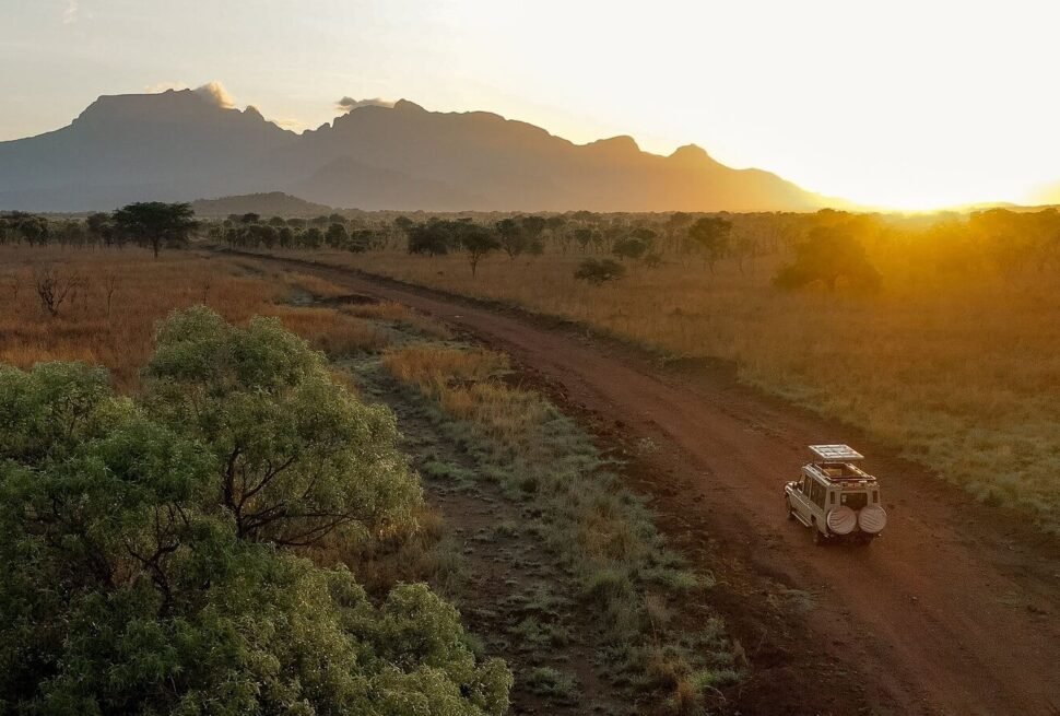An aerial view of a safari vehicle driving along a dirt road through the misty hills of Bwindi at sunrise.